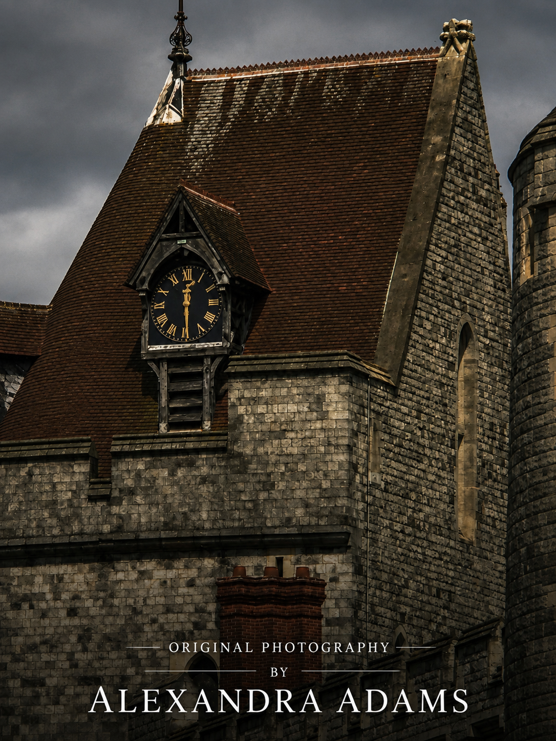 Dark moody photograph of a stone building with a steep brown tiled roof, a small clock face, and a cloudy sky. Text at the bottom reads 'Original Photography by Alexandra Adams'.