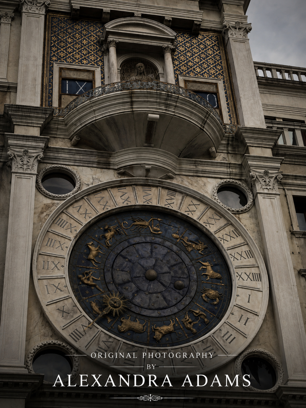A dramatic low-angle photograph of the ornate astronomical clock face on a historic stone building facade, featuring gold zodiac symbols on a dark blue circular dial. Text at the bottom reads 'ORIGINAL PHOTOGRAPHY BY ALEXANDRA ADAMS'.